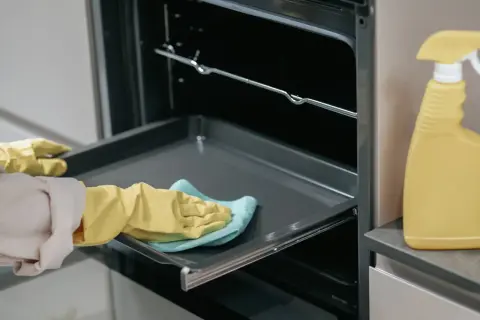 Rękawiczki i ściereczka pomagają w tym, jak wyczyścić blachę z piekarnika. Obok stoi żółta butelka ze sprayem.