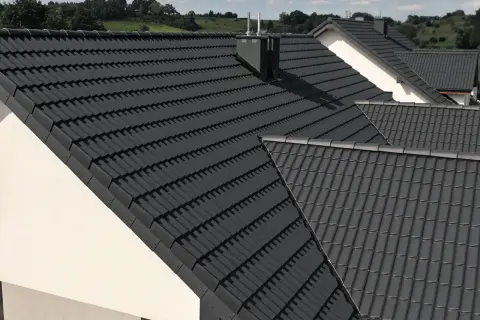 Szare, nowoczesne dachy betonowe pokrywają domy na tle zielonych wzgórz.